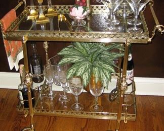 Ornate brass res cart/ bar. On wheels. Glass shelves. Six brass bottle holders.