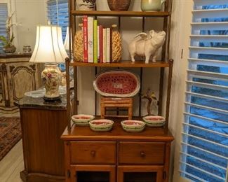 Nice baker's rack, with hand-painted Italian porcelain watermelon serving set, cast iron piggy that can fly, assorted cookbooks, vintage hand-painted china pitcher, hand-painted Portuguese earthenware pitcher and pottery vase.