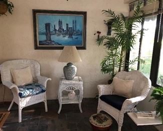 White wicker chairs, lamp table, lamp, wall art and one of many faux trees and plants