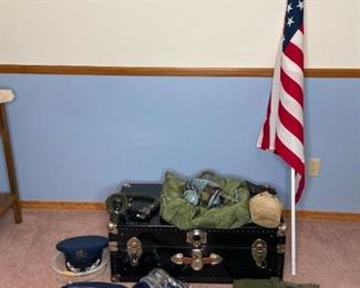 Metal Trunk with Military Items
Black metal trunk in great condition except one of the latches is bent but still latches. Pilot headset (one of the ear pieces is broken), breathing apparatus, parachute material bag, A-bag, canteen, ties, suspenders, hats, belts, and medals, American Flag on aluminum flag
