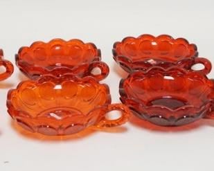 1095	7 RUBY RED FOSTORIA COIN GLASS CANDY DISHES, LOT INCLUDES 6 SMALL HANDLED DISHES & ONE LOW COVERED CANDY DISH (HAS SOME MINOR INNER RIM CHIPS) 6 1/4 IN DIAMETER 

