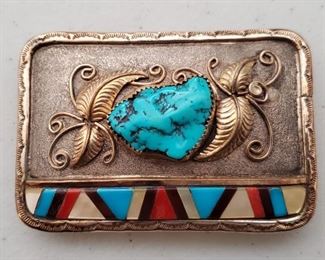 Navajo Sterling 12k Belt Buckle Alvin Vandever. Sterling belt buckle inlaid with turquoise, mother of pearl, coral, and one other stone. The artist has applied a 14k gold finish to the leaf and scroll design and border. 2" tall and 3" wide. Signed A. Vanderver (this well known artist's name is Alvin Vandever, but his name was misspelled for a long time on his stamp before it was noticed). Also inscribed "Inlay by E.B.".