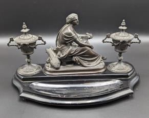 Antique Bronze Inkwell with decorative urn inkwells and center figurine.

 There are scratches/damage on the wood base and the middle sculpture is loose and needs to be tightened. Measures 7” x 14” and 8” high.