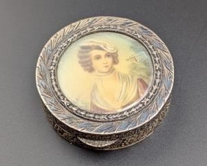Sterling Silver (800) Portrait Trinket Box. The outer rim of this trinket box features a lovely raised relief design. There is bubble on the top portrait that can be seen in the photos. Marked 800 and measures 1.75” in diameter and .5” high.