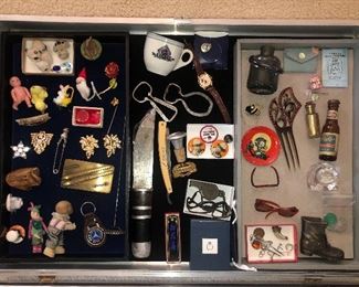 Display case items: Vintage dress clips, tiny animals, Alaska Steamship Co. cup, advertising bottle openers, Peora amber pendant, Erik Höglund bottle, glass troll, doll sunglasses