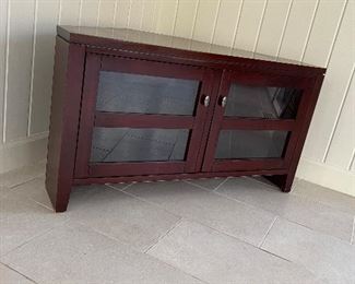 Corner TV Stand with glass front cabinet doors. Dark Cherry wood MDF. Height: 24". Depth at center: 24". Width across front: 44". PRICE $ 75
