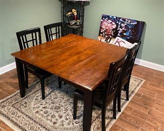 Solid wood kitchen table with four chairs has drop down hidden leaf. Iron wine holder. Poker Art.  Neutral tones area rug