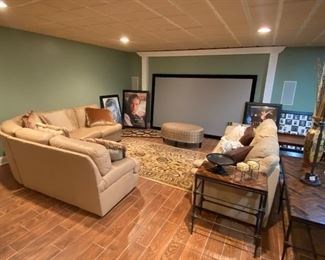 Beige color three-piece leather sectional. Beige color full size leather sofa.  Extra large projection screen. Framed movie posters. Several area rugs. 