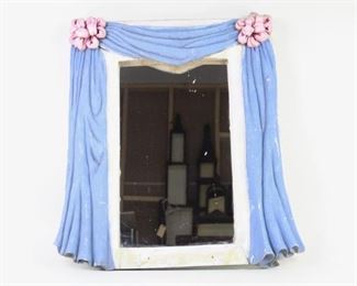 Lot 26: Hand Made Folk Art Mirror w/Draped Frame. Fun theatrical folk art mirror with a frame made in plaster. Gray white base frame with a blue drape with pink bows covering the top and sides.

Dimensions are 27.5 in h x 26.5 in w x 3.5 in d. Condition is fair to good. Discoloration and dirt on frame. Some paint loss and cracks, and scuffs. Repair to bottom and back. Heavy. Please call or email for a detailed condition report.