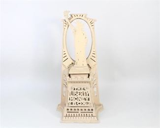 Lot 34: Carved Wood Folk Art Statue of Liberty Money Box Bank. Hand-carved "Liberty Money Box" depicts the Statue of Liberty atop a decorative podium with escutcheons on its sides and intricately detailed borders and trim. A rear ovular frame further highlights Lady Liberty, at whose feet one is supposed to place coins, through a slot emptying into podium. Hinged door at rear for access to interior.

Dimensions are 13.5 in h x 6.75 in w x 4.5 in d. Condition is very good, with minor surface wear and spots of paint loss. Missing small screw in back that keeps door closed. Please call or email for a detailed condition report.