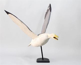 Lot 49: Carved Wood Duck/Seagull American Folk Art Sculpture. Wonderful bird sculpture is in flight, with wings lifted and open mouth tilted down. Carved with initials TLA on the underside and carved in Maine. Full of life and character, on a new stand for display. From the collection of Barbara Porter & Robert Wincuinas.

Dimensions are 41 in h x 41 in w x 32 in d. Condition is good though there is a chunk broken out of the tail. Please call or email for a detailed condition report.