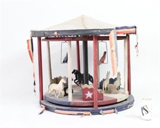 Lot 67: Large Patriotic Hand-Painted Folk Art Wood Carousel. Handmade carousel measures 27.5 inches in diameter and 26 inches high. Complete with three pairs of horses and passenger booths, and two birds hanging from above. All decked out in red white and blue, painted stars, and paper trim adorning some edges. Animal figures have a charmingly soft-edged, primitive form.

Dimensions are 26 in h x 27.5 in w x 27.5 in d. Condition is fair, with delicate paper trim significantly worn and some small cracks in wood. Please call or email for a detailed condition report.