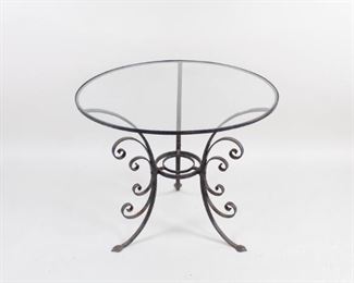 Lot 72: Wrought Iron Scrollwork Round Glass Top Outdoor Table. Wrought iron base and legs have a decorative scrollwork shape, adding visual interest that can be viewed through the inset glass tabletop. A nice addition to any garden, patio, balcony, or other outdoor area that will last for many more years.

Dimensions are 27.25 in h x 30.25 in w x 30.25 in d. Condition is good, with surface wear and oxidation to metal base. Please call or email for a detailed condition report.