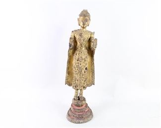 Lot 112: Standing 24-in Gilt Metal Glass Inlay Buddha Sculpture. Gilt painted metal (possibly bronze) with intricate inlay in what appears to be glass. Buddha stands on 4-tiered lotus pedestal with both palms up in double abhaya mudra, also known as the gesture of reassurance. Elaborate decoration and royal costume is characteristic of Thai Buddhist imagery, though this piece is said to have come from India. Includes hooks on back for securing or mounting to wall.

Dimensions are 23.25 in h x 5.75 in w x 6 in d. Condition is fair, with surface wear throughout, paint and inlay loss, and some small fragments that appear broken off. Please call or email for a detailed condition report.