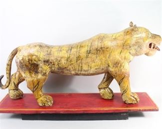 Lot 143: Large Wooden Carved & Painted Indian Tiger Sculpture . A carved sculpture, beautifully painted displayed on a red painted platform. Carved out mouth with teeth and tongue sticking out. Weathered with a wonderful patina. Acquired in the 1980s, India. From the collection of Barbara Porter & Robert Wincuinas.

Dimensions are 24 in h x 42 in w x 9.5 in d. Condition is fair to good. Paint chipping and fading throughout. Cracks along the body, legs and tail. Some discoloration. Please call or email for a detailed condition report.