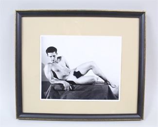 Lot 210: Framed Original Bruce of LA B&W Gay Nude Male Photo. B&W photo by legendary Bruce Bellas of LA shows a nude man reclining on a draped pedestal, and is framed in black & gold. From the collection of contemporary artist Cary Leibowitz. Please note that the black box is for this internet posting and is not on the photograph.
Dimensions of the frame are 13.5 in h x 15.75 in w x 1 in d. Condition is very good with minor wear to the frame. Please call or email for a detailed condition report.