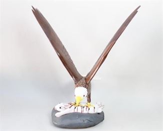 Lot 260: Carved & Painted Wooden Bald Eagle Folk Art Sculpture. A large wooden sculpture from Maine of a bald eagle capturing a rabbit. Finely detailed wings and head. The beak is painted in a glossy enamel type paint and contrasts nicely against the head. Plastic bead eyes on both eagle and rabbit. From the collection of Barbara Porter & Robert Wincuinas.

Dimensions are 42 in h x 36 in w x 29 in d. Condition is good. Some surface wear and discoloration, most notable on tail feathers. One or two millimeter space between wings and body. Minor paint chipping in some spots. Please call or email for a detailed condition report.