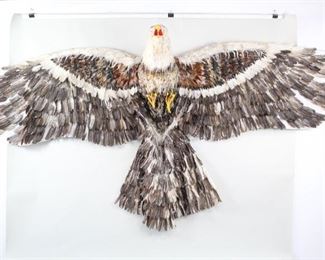 Lot 272: Larger Than Life Bald Eagle Folk Art Wall Sculpture. A massive bald eagle sculpture, in fact a kite, though it was never used as such. Made with real feathers attached to fabric over a slender wood structure make out the wings and tail, while the body and head is built up with papier mache. An impressive piece that looks great on a large wall or hanging from a ceiling. Acquired in the 1990s, Indonesia. From the collection of Barbara Porter & Robert Wincuinas.

Dimensions are 72 in h x 149  in w x 24 in d. Condition is fair. Surface wear. Missing feathers. Remaining feathers in good to poor condition. Fragile. Please call or email for a detailed condition report.