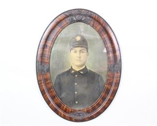 Lot 487: Framed WWII American Military Photograph of a Solider. A handsome hand colored portrait of a young WWI-era soldier. Mounted in an oval frame that is carved with two American flags on either side and emblems at top and bottom and painted with a faux wood grain.

Dimensions are 25 in h x 18.5 in w x 1.25 in d. Condition is good. Light wear to frame. Please call or email for a detailed condition report.