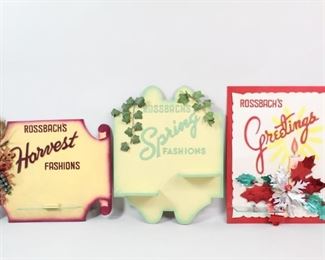 Lot 497: 3 Rossbach Fashion Store Display Advertisement Signs. Three 1950s seasonal display signs from Rossbach fashion department store; spring, harvest and a seasonal greetings signs for Christmas and winter holidays. The harvest and seasonal greetings sign both have one, clear glass shelf attached while the spring has two in wood, painted in the same colors as the back board. Comes with their original shipping boxes.

Dimensions for the smallest are 21 in h x 27 in w x 2.5 in d. Dimensions for the largest are 28 in h x 22 in w x 4 in d.Condition is very good. Minor surface wear. Please call or email for a detailed condition report.