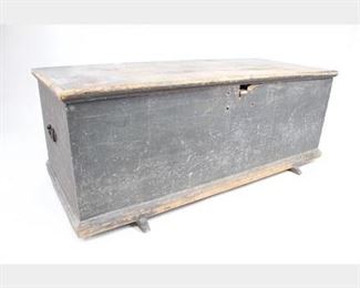Lot 299: Primitive Antique Painted Storage Blanket Trunk Chest. Beautiful wooden chest has been painted long ago a gray/blue/green, which now has been worn, leaving a lovely patina. Lid is attached with wrought iron hinges with wrought iron nails; however there are also modern screws..perhaps a more recent repair.  Dimensions are 19 in h x 48.75 in w x 20.5 in d. Condition is good with surface wear, worn edges and paint, some stain spots, missing a side handle, and some of the edges of the lid is loose. Please call or email for a detailed condition report.