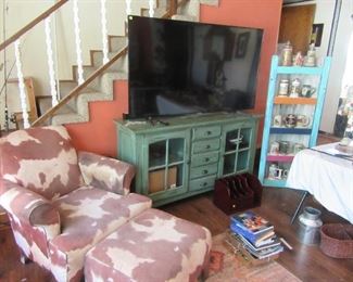 Cow pattern chair and ottoman, Large screen TV , books, beautiful server that TV is setting on.