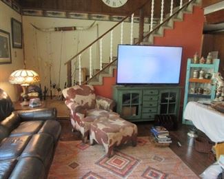 Living room shot. Leather (electric) couch and chair, rug, faux cow print chair and ottoman. Lamps and tables full of collectibles.