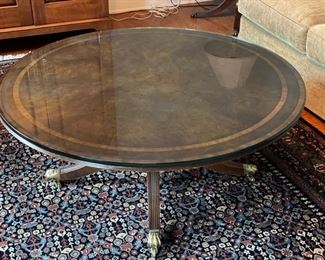 Arthur Brett glass-topped pedestal cocktail table with satinwood banding and brass feet. Measures 44.5" D.