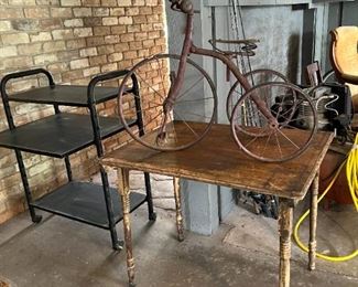 Antique metal tricycle; small wooden table; computer desk on rollers