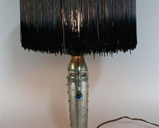 1	Art Deco Style Lamp With Tassel Shade	"Art deco style metal table lamp with tassel shade. Signed ""Pen Ves (?) 72 V..a 1993"" on base. Shade does not sit squarely on top of base. 
21"" H x 5 1/4"" Base diameter."
