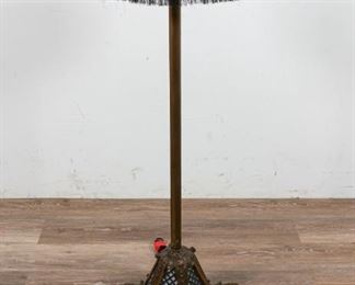 15	Art Deco Floor Lamp and Stand	Art deco floor lamp and stand. Metal lamp base with openwork shade, paper to the interior. Metal table top with fabric fringe. 42" H (from base to top of stand). Indentation to table's surface. Crack to metal appliques on the lamp.
