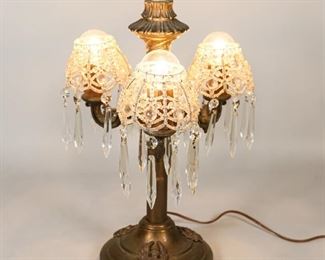 54	Calpa Brass Candelabra Lamp	Calpa brass 3 arm candelabra lamp. With putti motif base and later center arm and finial. With 3 beaded crystal shades. Marked on the underside Calpa 110. 17 1/2"H. Losses and wear to patina throughout, base dented near cord.  Beaded shades sit on round lightbulbs.
