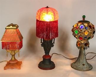 69	3 Boudoir Lamps	"3 boudoir lamps. Pink glass with beaded brass overlay shade, 9 1/2""H including shade; patinated metal lamp with openwork shade with colored glass facets, 13 1/4""H with finial; painted metal lamp with cranberry glass shade with silk fringe, 15 1/4""H with finial. 
Pink lamp shade repaired at corners, missing fittings to hold shade in place; patinated metal lamp with losses to patina on base and shade, cap and shade bent, shade does not sit evenly on lamp; cranberry glass lamp losses to paint decoration, crazing around handles, finial crooked on shade, wear to glass shade."
