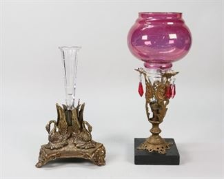 71	2 Epergnes	"2 epergnes. Brass and glass epergne mounted on a stone base. Round pink trumpet with hanging crystals. Gilt brass epergne with swans. Single glass trumpet with etched flowers. Pink glass epergne: 4 1/4"" L x 4 1/4"" W x 14"" H.  Wear to pink glass trumpet, brass loose to bottom of pink trumpet. Chip to glass trumpet of swan epergne. 
"
