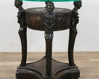75	Carved African Style Side Table	"Carved African style side table. Late 20th Century. Glass top with tassel center, carved African figural supports, wicker top and base. Some slight wear on figural supports, wear to glass top. 
25 1/2"" H x 20"" diameter"
