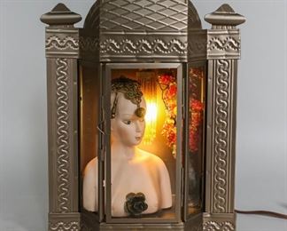 99	Found Object Lamp	Found object lamp. Porcelain female bust with metal appliques to the head and chest. Beaded light with metal tree and beaded grapes. Hammered metal cabinet with three glass panels. Metal latch to left side of door. 9" L x 4" W x 12" H. Paint residue to lower center of case.
