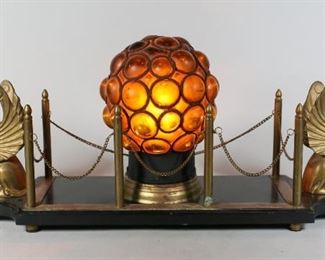 105	Art Deco Griffin Caged Glass Lamp	Art Deco caged amber glass lamp mounted on a hardstone base with patinated metal griffins. 25 1/4" L x 6 1/2" W x 10" H. Scuff to the base, later painting to the metal inlay of the base. Rust present to amber shade.

