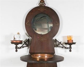 132	Italian Folding Shaving Stand with Mirror	Italian wood shaving stand with fold out table holding a copper basin, 2 iron folding arms holding a porcelain shaving mug with brush, orange iridescent glass cup. Mounted copper candle holder on top of the stand. Inset mirror with iron mounted whales around the outside. Marked with metal tag to the clasp, Made in Italy. 24 1/4"L (table folded out) x 17" W 42 1/2"H. Crack to wood mirror panel, later mirror installed. Wormholing to wood throughout.
