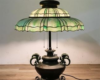 140	Bradley & Hubbard Cast Iron Dragon Kerosene Lamp	Bradley & Hubbard cast iron dragon table lamp with green slag glass shade. 1st quarter of the 20th century. Electrified kerosene lamp. Raised knob on lamp marked B & H. 35" H (from base to finial) x 26 1/2" shade diameter. Wear to paint on body of lamp, wear to paint on feet, scuffing to body of lamp.
