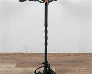 164	Wrought Iron Candle Stand	Wrought iron candle stand. Floral stand with 4 candleholders, later added flower finial and bronze putti. Top repaired near finial. On top a coiled stand with 4 feet. 13" L x 13" W x 38" H. Repair to floral top. Wear to paint on putti. Putti loose in stand. Rust present throughout.
