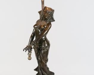 177	Egyptian Revival Bronze Nude Lamp	20th century Egyptian revival bronze nude, unsigned. Mounted on a wood and metal lamp base, with floral metal shade. 25"H to top of shade, bronze 12 1/2"H. Both hands on bronze repaired, with later chains on wrists; wear, dents and discoloration to shade, wear and losses to lamp base.
