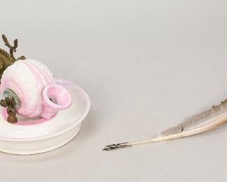179	French Porcelain and Brass Shell Inkwell	French porcelain and brass shell inkwell. Pink and white porcelain stand and shell, brass fittings with cameo. Feather with contemporary pen nib. Marked on the underside with red mark. 5 1/2" diameter. Flake to rim of dish.
