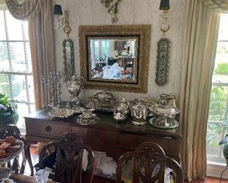 Wonderful selection of silver and silverplate. Also RARE and wonderful leather top buffet with fine details.  Also show are the beautiful shield back dining chairs with Prince of Wales Plumb and  graceful swags. The seats are prepared for custom fabric or use the chic updated slip covers on them. 