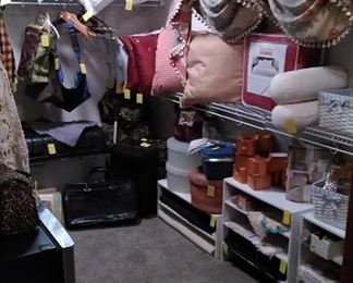 Closet full of decorative pillows, shoe shelves, valences, linens, suitcases and even a mini refrigerator with freezer.