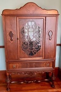 This REMARKABLE vintage cabinet measures 72x44x16 inches. This lovely cabinet features an intricately designed glass front door and drawer on the bottom for extra storage. There are some wood chips and wear but in overall good condition.