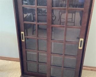 Dark colored wood-like display cabinet with (2) glass slider doors, (3) adjustable shelves, H 50"x W 33"x D 16". It has chips and scratches in numerous areas.