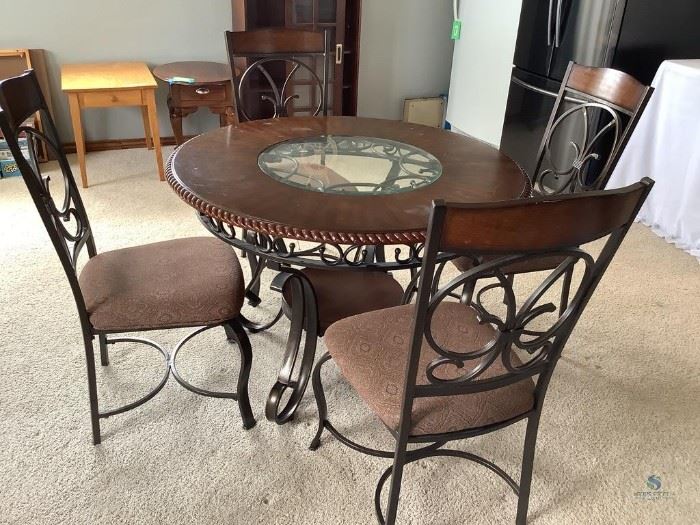 Dark wood and black decorative wrought iron round dining table, with glass in center of table top, some wear and scratches on the table surface. Also has a small lower shelf under the table. Comes with (4) matching chairs with cloth cushion seats, fabric shows some wear, lazy Susan, glass sugar, salt & pepper shakers and doily. Table H30"x W 45", chairs H 39.5"x W 19.5"x D 24".