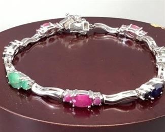 One rhodium plated sterling silver 7.5" bracelet set with 2 oval mix cut and 4 round mix cut emeralds, 2 oval mix cut and 4 round mix cut blue sapphires and 3 oval cut and 6 mix cut rubies in claws setting. 12gtw, with appraisal certificate included. Bracelet is 7.5".