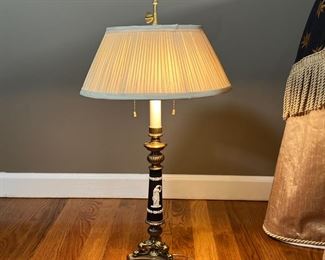 GREEK-STYLE TABLE LAMP | Brass tripod base supporting a black column with white raised laurel leaves and the figure of a woman holding a bird, having two light bulbs and chain pulls; overall h. 26 in.