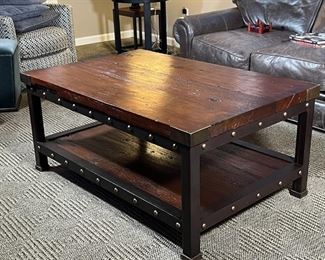 INDUSTRIAL COFFEE TABLE | Low table, having a dark wood board top and lower shelf with brass supports and tacks on a black metal block leg frame; h. 20 x 46 x 30 in.